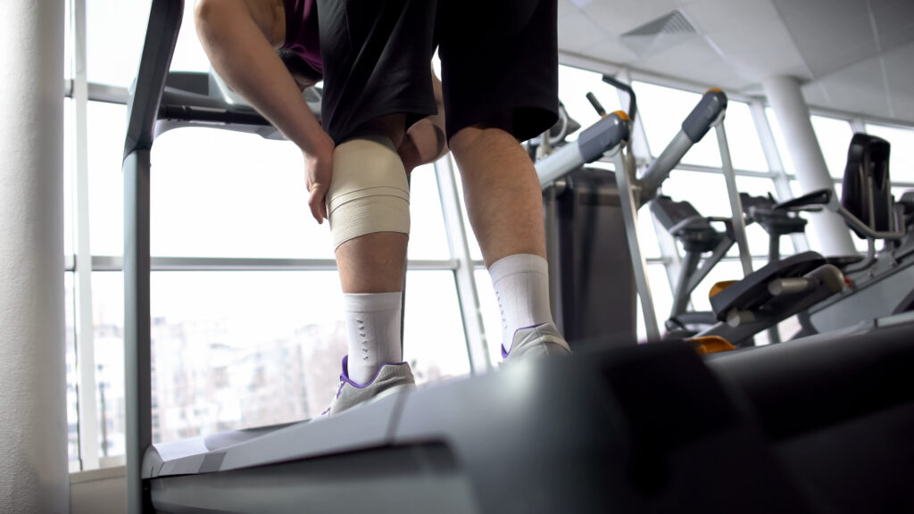 Man with calf bandage suffering from pain, standing on treadmill, rehabilitation