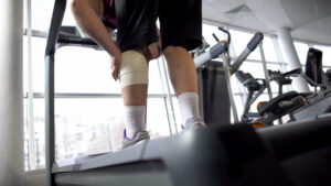 Man with calf bandage suffering from pain, standing on treadmill, rehabilitation